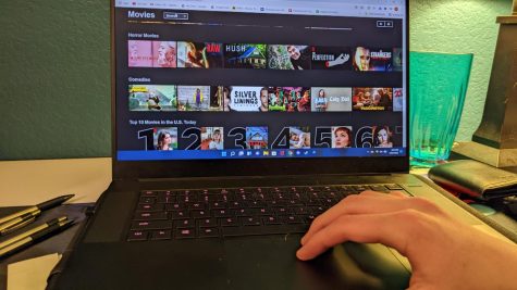 Hand on keyboard, scrolling through Netflix on a computer.